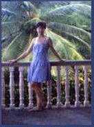 [A woman standing on the second 
floor of a veranda with a palm tree spreading its leaves behind her.]